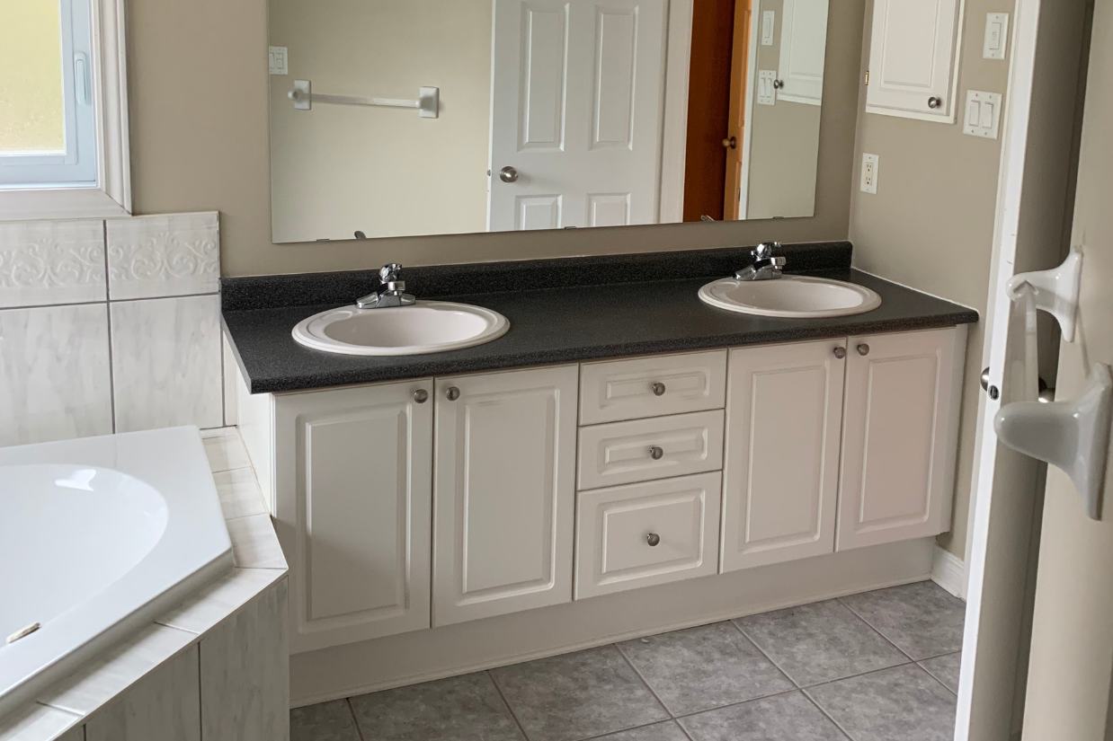 Before: Builder bathroom with white cabinet and corner tub.
