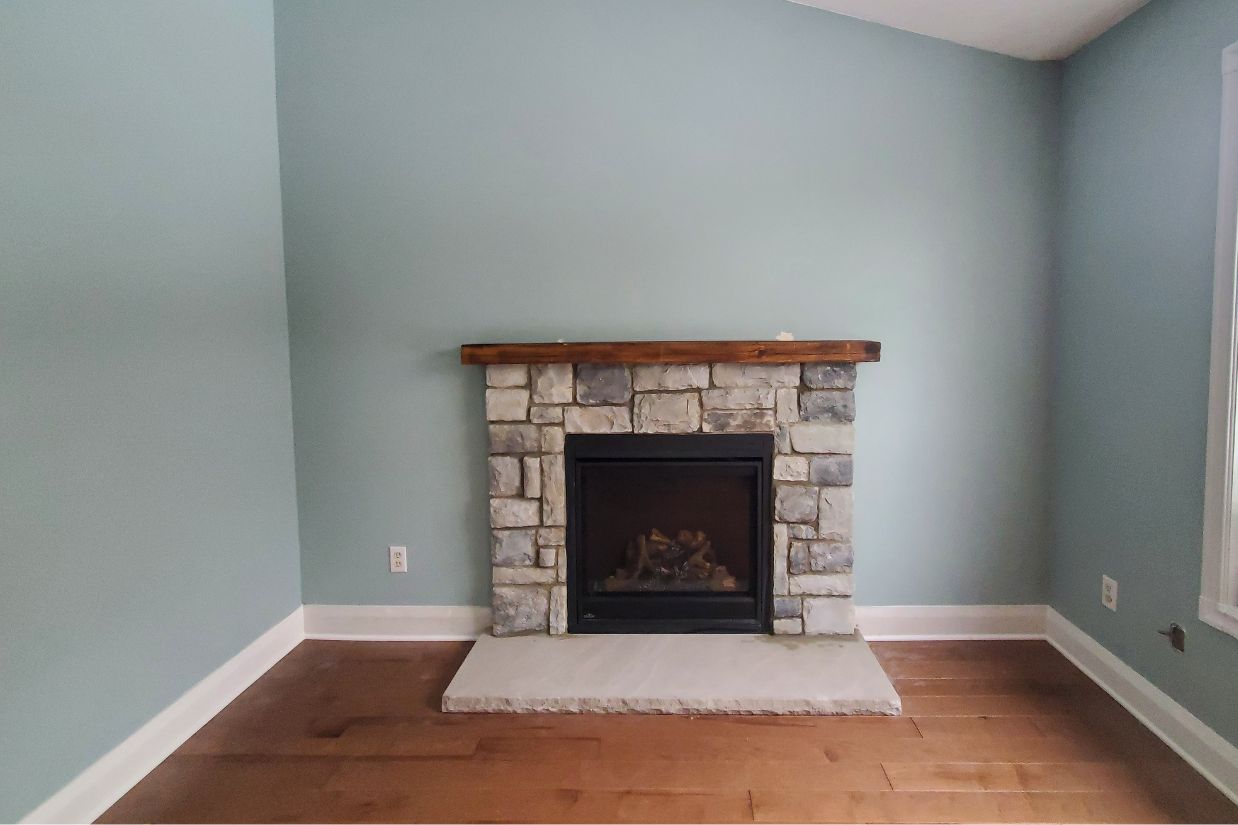 After: Grey stone fireplace with wood mantle and light blue wall.