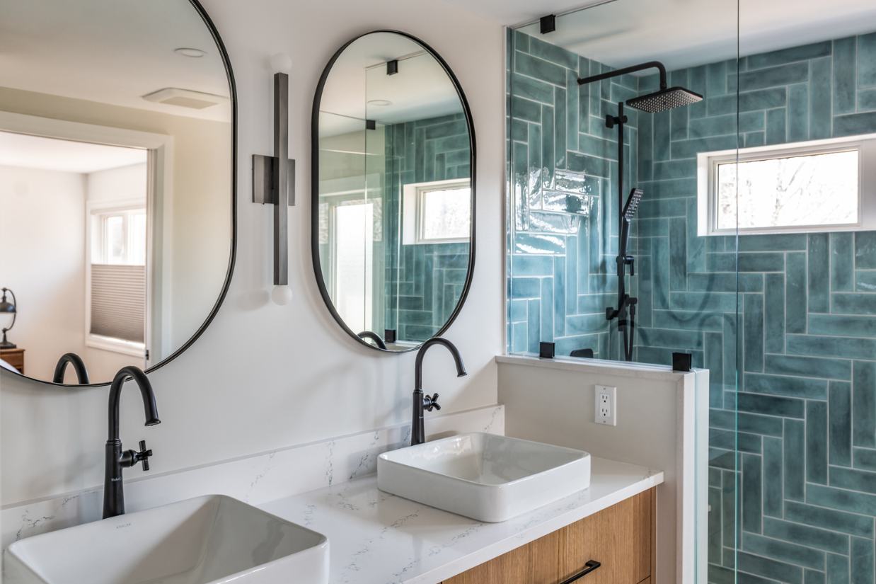 Two sinks on a natural wood vanity with a teal tiled shower in background.