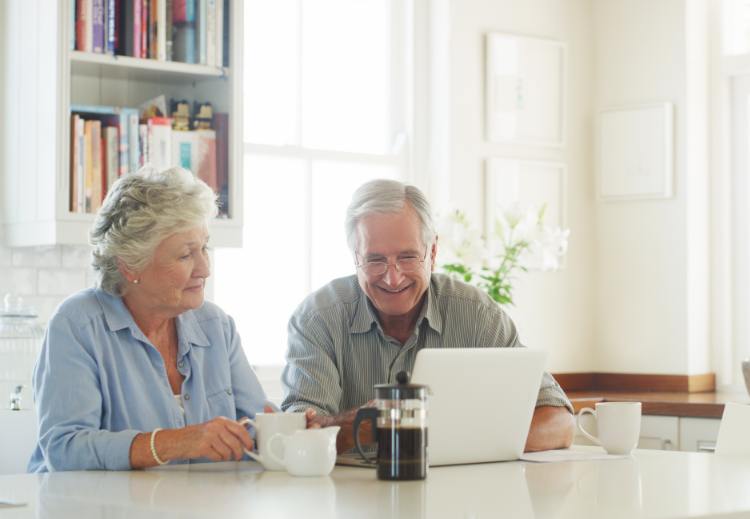 Two seniors looking at something on a computer while sitting in their modern kitchen.